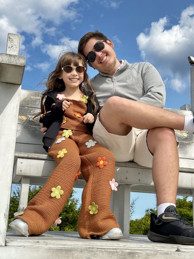 The brother and sister behind JMM Florida, smiling in sunglasses on a white wooden bench under a blue sky